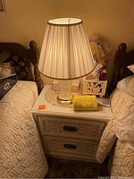 Nightstand between beds showing the glass lamp with pleated lampshade on top and other small items