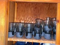 Shelf with clear glass tumblers featuring dark gray plastic holders, 10 pieces total.