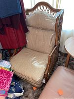 Front and side views of rattan chair with beige cushions wrapped in plastic. Chair is positioned against a window with natural light.
