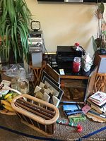 Wide angle showing end table with Panasonic VCR on top, framed art leaning, fake palm tree, and additional household items including candles and books nearby.