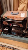 Vintage black Singer sewing machine with ornate silver detailing, in open worn carrying case with blue handle.