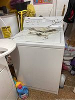 Full front and right side view of the white Kenmore 600 series washing machine in a laundry area with items on top and around it