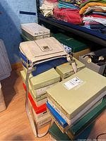 Stack of shoe boxes with shoes inside visible. Beige faux leather bag on top of the boxes.