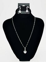 Full view of necklace with heart-shaped pendant and matching earrings on a black display bust.