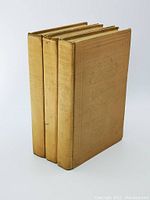Photo showing three beige cloth hardcover volumes standing side by side with embossed titles and crests on spines and front covers.