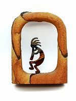 Front view of Kokopelli figure in sandstone arch sculpture, showing textured sandstone with patterning and metal figure with detailed polished finish.