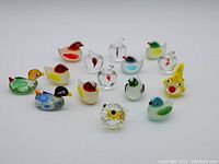 Photo showing entire collection of 15 miniature glass figurines including ducks, birds, fish, and apples with varied colors and styles.