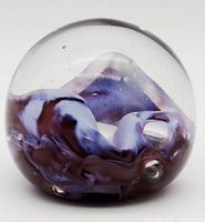 Clear spherical glass paperweight with swirling purple and lilac ribbons and embedded bubbles inside.