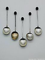 Group photo showing 5 vintage sterling silver coffee spoons with black bakelite coffee bean detail on handle ends, various solid and one slotted spoon bowl.