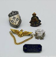 Four vintage military pins laid out on white background showing details and markings