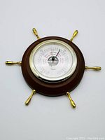 Full front view of the vintage barometer in ship wheel style wooden frame with gold handles.