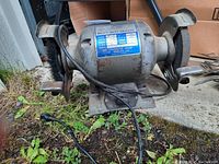 Side view of the grinder showing the left grinding wheel, motor housing and power cord on concrete and grass area.