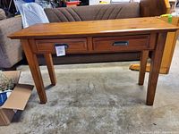 Front view of Ashley Furniture wooden sofa table showing two drawers and tapered legs with a price tag attached.