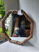 Octagonal wall mirror with rustic wood-look frame standing upright on a white surface, showing its reflective surface and textured frame details.