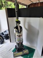 Front view of Bissell Pet Hair Eraser Turbo vacuum upright with clear canister and green accents, on green mat and white backdrop.