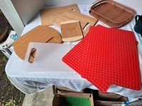 Photo showing 3 wooden cutting boards, 1 clear plastic cutting board, 2 red silicone drying mats, and 1 brown plastic tray arranged on a white tablecloth.