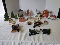 Front view of the wooden village pieces and figurines arranged on a white surface, showing houses, trees, church, barn, and animal figures.