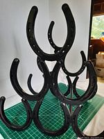 Front and side angles of a black metal horseshoe wine rack on a green cutting mat with a white backdrop.