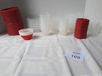 Photo showing several stacks of small, medium, and large Tupperware containers with red lids and translucent white bases, arranged on a white cloth background.