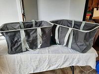 Two charcoal collapsible totes sitting open on a table showing exterior sides and handles