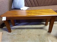 Side view of one wooden dining bench showing solid wood construction and square legs.
