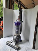 Full view of the upright purple Dyson Animal vacuum cleaner assembled and standing upright on a white surface with a white photo backdrop.