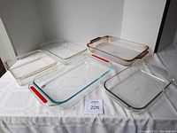 Five glass bakeware dishes arranged on a white cloth including two Pyrex with red handles and three varied glass dishes