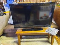 Front view of Samsung 40-inch flat screen TV on stand with accessories in sealed plastic bag on wooden table.