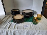 Full view of stacked sets of dinner plates, salad plates, soup bowls alongside two handblown green ombre glasses on white cloth background.