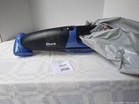 Side view of the blue and charcoal Shark cordless handheld vacuum with attached nozzle, placed on a cloth surface.