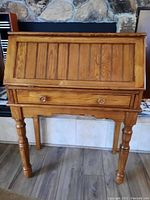 Front view of oak secretary desk with drop-down door closed, showing paneled wood design and turned legs.
