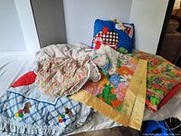 Overview of multiple vintage baby blankets and quilts piled together showing colors and patterns