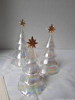 Photo showing three iridescent Lenox glass Christmas trees with gold star toppers, arranged on a white surface.