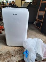 Front view of white Vremi unit standing on garage floor with accessory bag to right