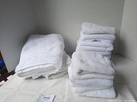 Stack of white plush towels including hand towels, bath towels, and wash cloths, neatly folded and stacked showing texture and condition.