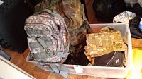 Two large camouflage backpacks and several smaller fabric cases and packs in a plastic bin