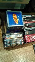 Top view of DVDs in cardboard box showing a Seinfeld DVD box set and various individual DVDs including Spider-Man and The Sopranos DVDs.