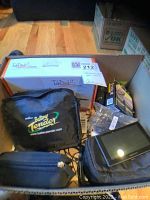 Box containing electronic car accessories including Battery Tender charger in case, Garmin GPS unit with mount, cables, and a box labeled TabDock2 Vision GPS bracket.