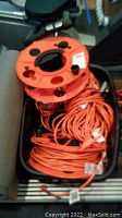 Four orange extension cords coiled together with plugs, and orange empty carrier reel in a black basket.