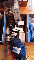 Box containing various health aids including knee pads in 5.11 Tactical packaging, TENS massager, Omron blood pressure cuff, and accessories.