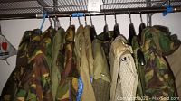 Rack of eleven garments including camouflage jackets, olive drab sweater, beige shirt, and black garment