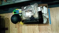 Box containing electronic items including cables, a white security camera, and miscellaneous wrapped components