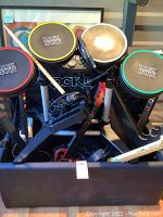 Full view of Rock Band drum unit on folding stand with four colored pads and foot pedal, cables visible over storage box