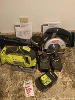 Photo of all three Ryobi cordless power tools (circular saw, angle grinder, and sabersaw) with three batteries and two operators manuals, arranged on a countertop.
