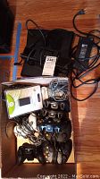 Box with multiple Xbox 360 controllers including black and white wireless models, and wired models with cables.