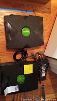 Top view of two original Xbox consoles showing their X-shaped design and green logos on top with cords and AC adaptors included.