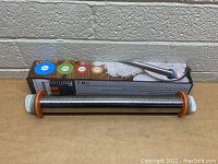 Front view of the stainless steel rolling pin with all four adjustable silicone rings attached on both ends showing the product and box behind it