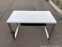 Front view of white office desk with metal legs, keyboard tray, and power strip
