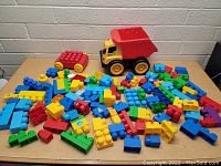 Large assortment of Mega Bloks building blocks on wooden surface against white brick wall.