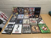 Photo shows a table with 20 DVD cases arranged in rows, cover titles visible.